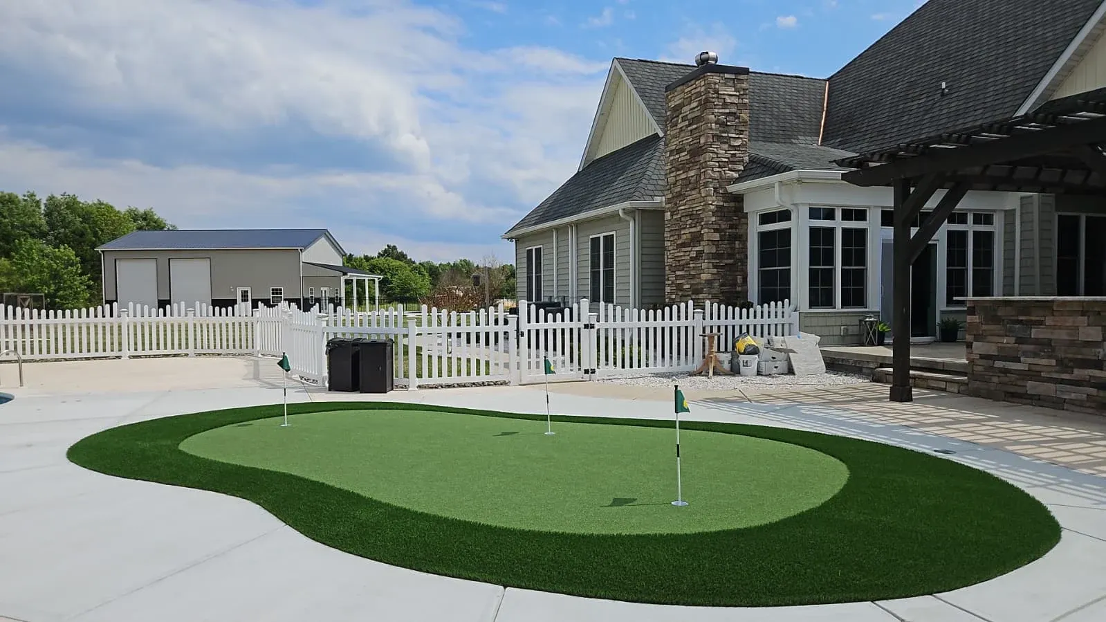 Three-hole artificial turf putting green beside a pool deck and stone patio