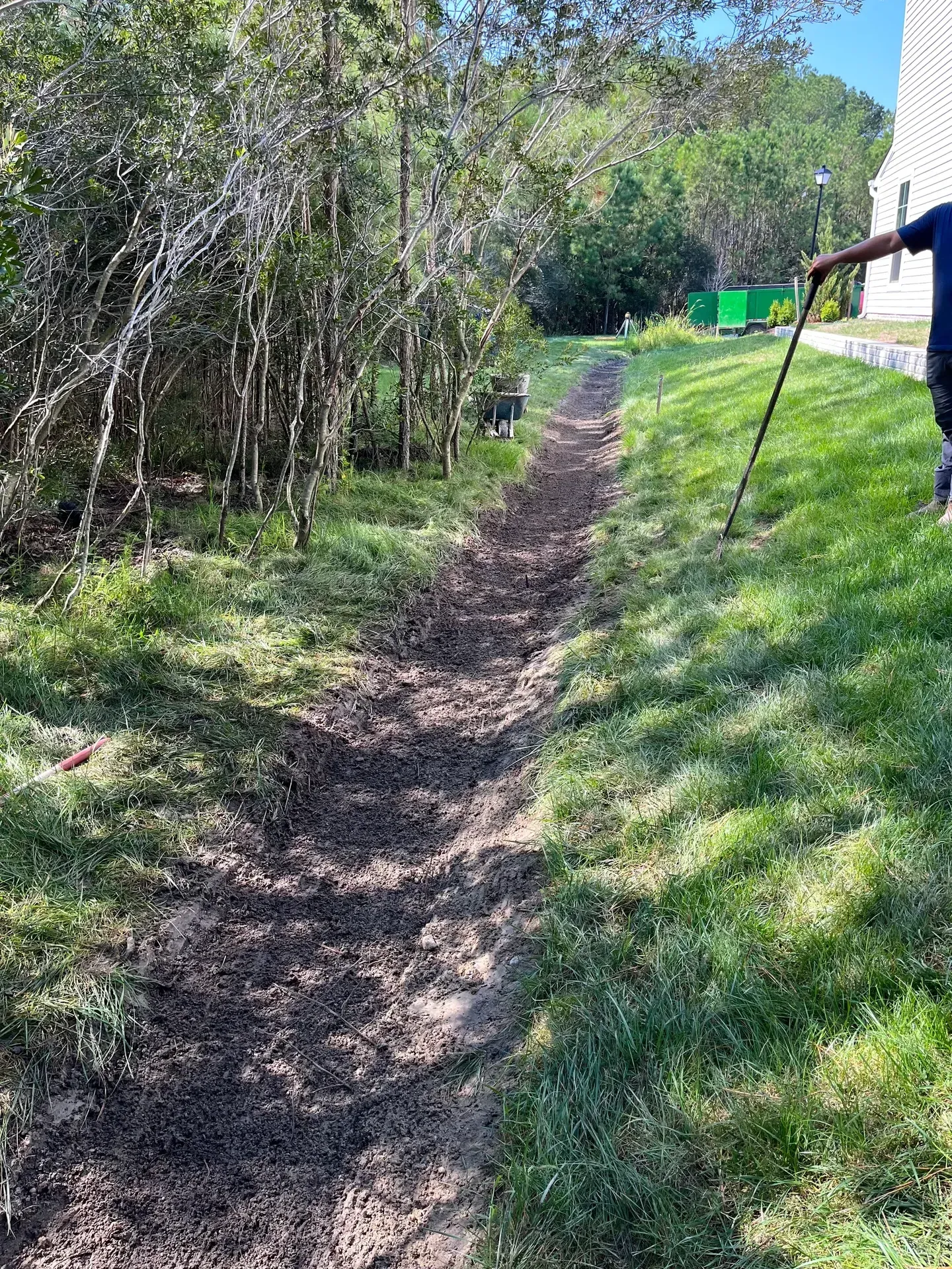 Freshly dug drainage trench running along a lawn at the edge of the woods