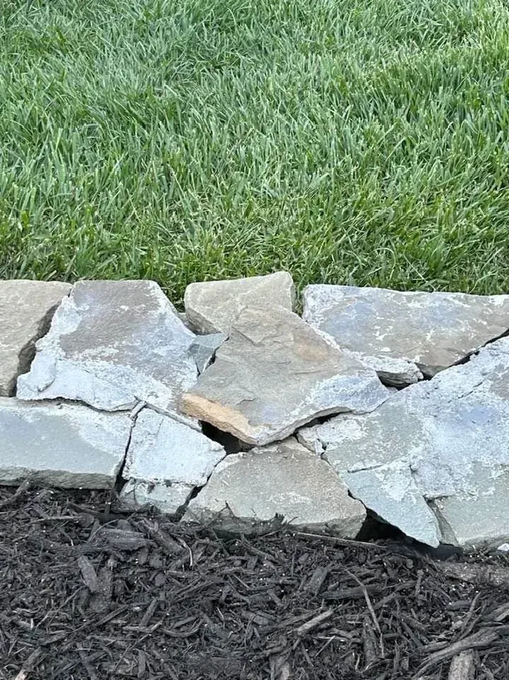 Natural fieldstone border separating a lawn from a black mulch bed