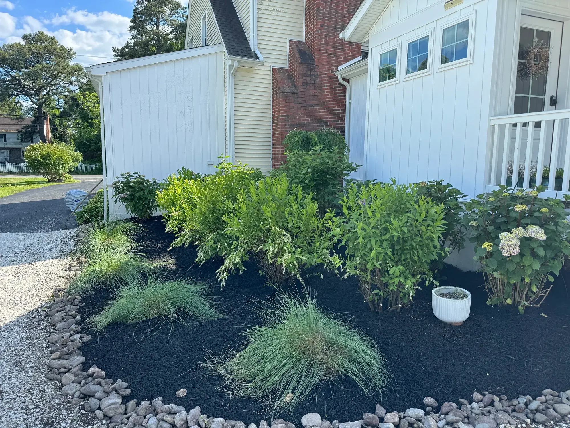 Front planting bed with shrubs, ornamental grasses, and hydrangeas in black mulch, edged with river rock