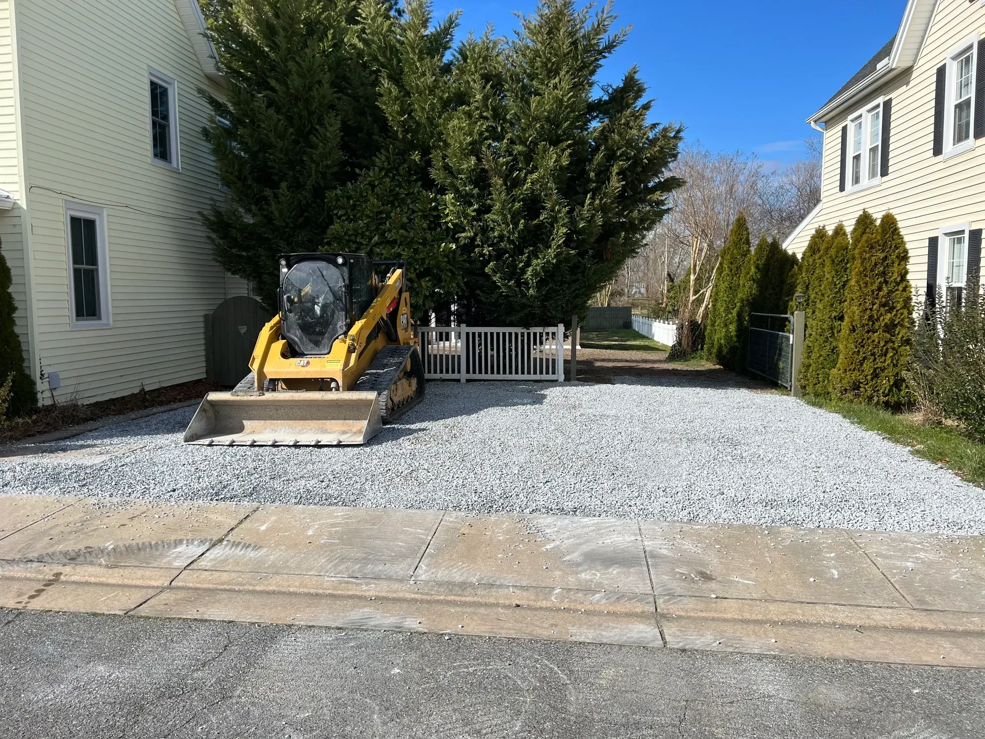 New gravel driveway with a compact track loader parked on it beside a house