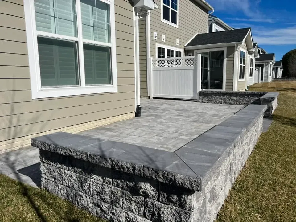Gray paver patio framed by a capped block seat wall behind a home
