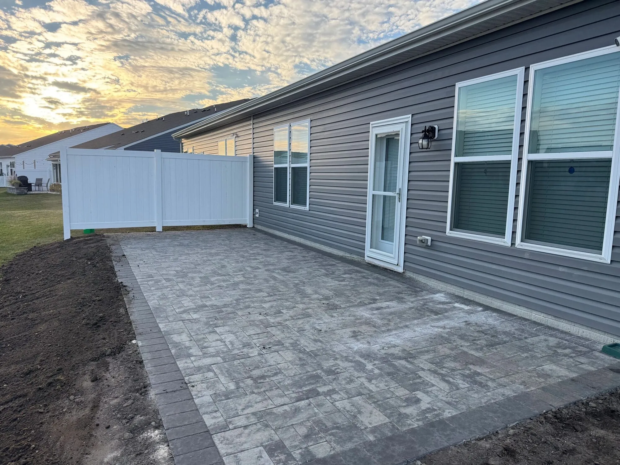 New gray paver patio running along the side of a house