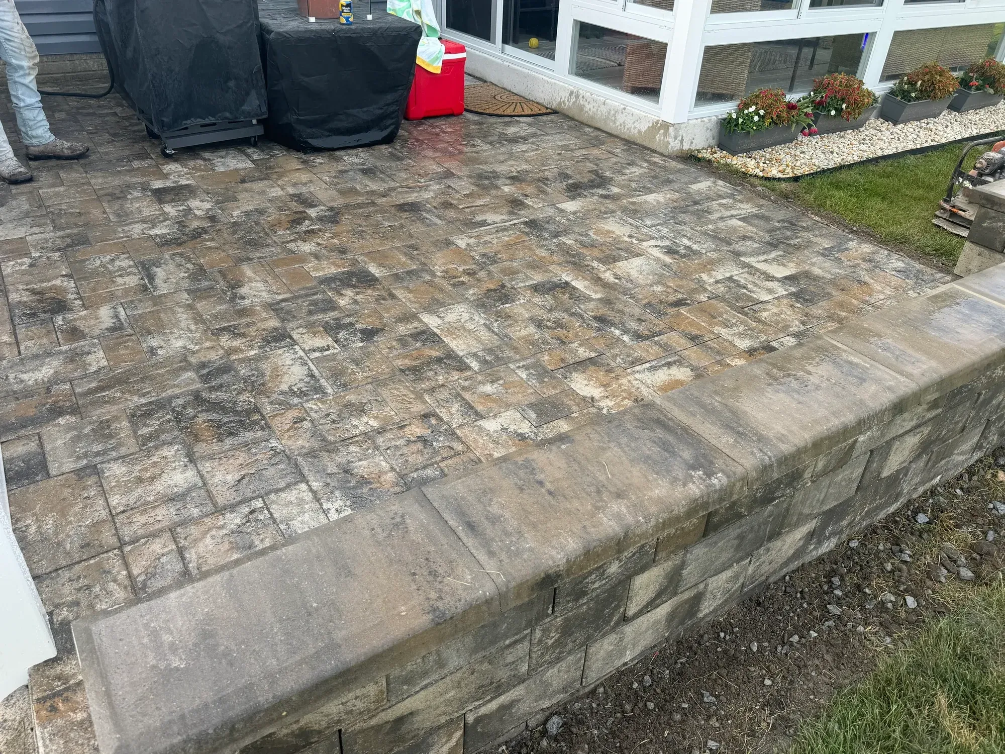 Raised multi-tone paver patio with a capped block wall beside a sunroom