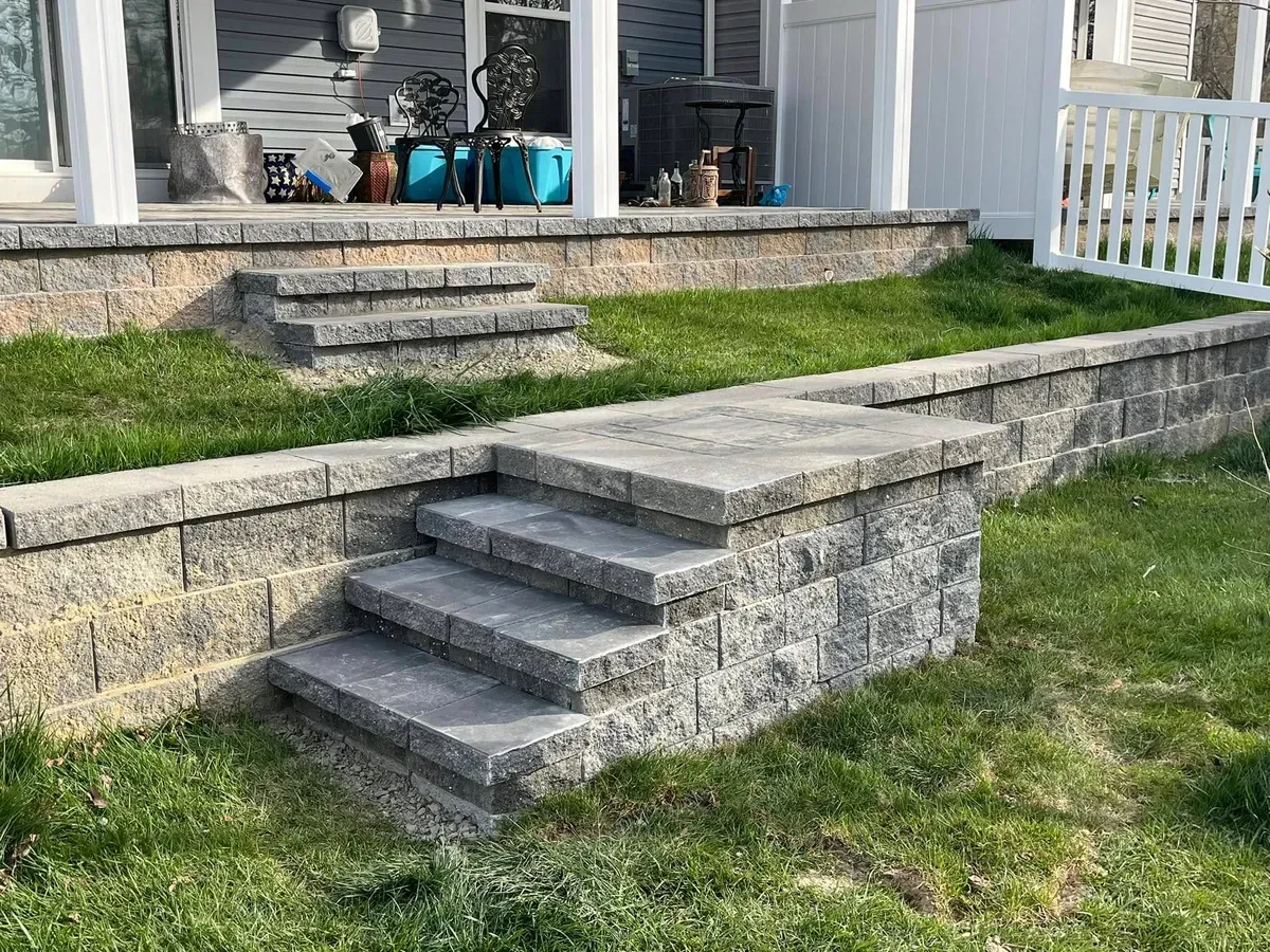 Block retaining wall with built-in paver steps leading up to a raised patio